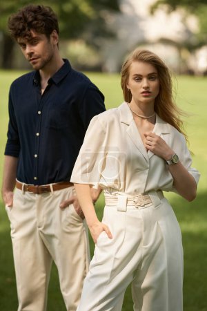 A stylish young couple in elegant attire standing in a lush park, exuding an air of old money sophistication.
