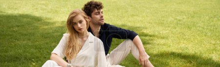 Una hermosa pareja joven con un atuendo elegante se sienta junta en un campo verde, exudando un estilo de dinero antiguo y disfrutando de un estilo de vida lujoso.