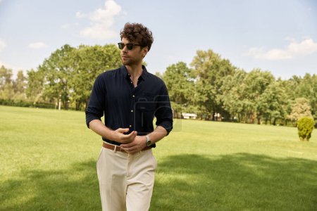 Téléchargez les photos : Un homme en chemise bleue et pantalon bronzé profite d'une promenade tranquille dans un champ vert luxuriant sous le vaste ciel ouvert. - en image libre de droit