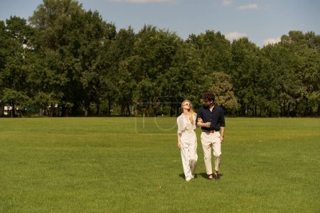 A beautiful young couple in elegant attire taking a leisurely walk together in a picturesque park setting.