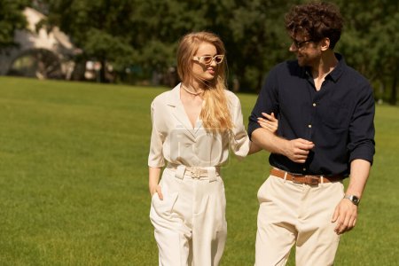 Una hermosa pareja joven en ropa elegante camina juntos en un campo verde, encarnando un estilo de vida lujoso y antiguo.