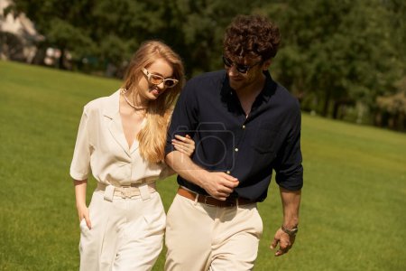 Ein schönes junges Paar, elegant gekleidet, spaziert gemächlich durch einen Park auf einer grünen Wiese.