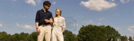 Ein schönes junges Paar in eleganter Kleidung, das anmutig auf einem saftig grünen Feld steht und einen luxuriösen Lebensstil der Elite verkörpert.