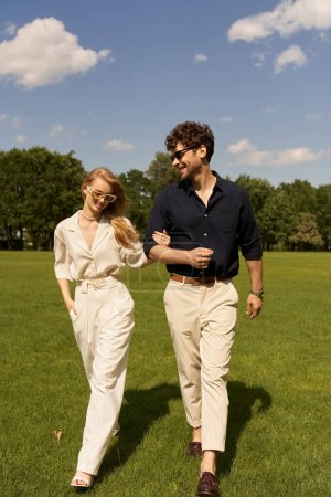 A man and woman, dressed elegantly, leisurely walking together through a vast green field.