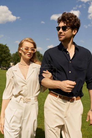 Un beau jeune couple en tenue élégante se promène tranquillement dans un parc luxuriant, incarnant un style vieil argent et un mode de vie riche.