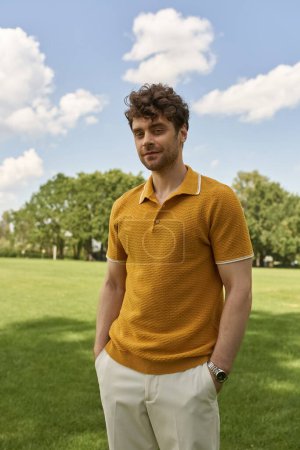 A man in a yellow polo shirt stands confidently amidst the lush greenery of a field.