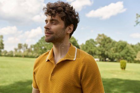 Foto de Un hombre, vestido con una vibrante camisa amarilla, se encuentra confiado en un vasto campo lleno de exuberante vegetación bajo los soles cálido resplandor. - Imagen libre de derechos