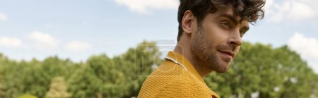 A man in a yellow shirt gazes confidently away in an outdoor setting, exuding style and charisma.