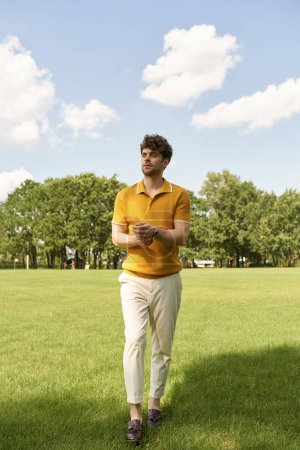 A stylish man in a vibrant yellow shirt stands gracefully amidst the lush greenery of a grassy field.