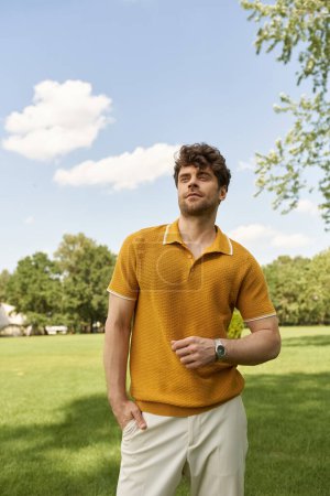 A man in a vibrant yellow polo shirt stands elegantly in a lush green field under the warm morning sun.