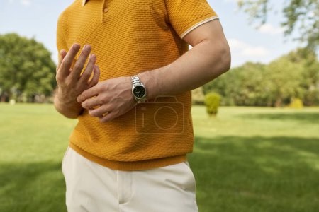 Ein Mann im gelben Hemd steht elegant in einem üppigen Park und verkörpert alte Geld-Eleganz und luxuriösen Lebensstil.