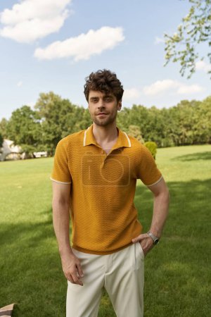 A man in a yellow polo shirt stands elegantly amidst a lush green field under the radiant sun.