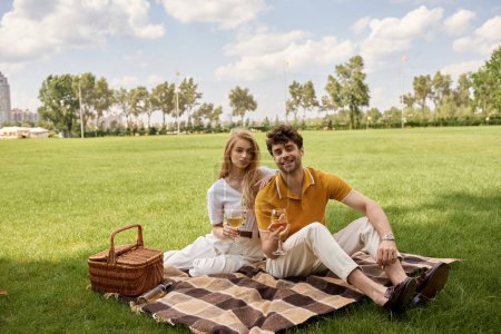 Stilvolles Paar in eleganter Kleidung bei einem luxuriösen Picknick auf einer grünen Wiese im Park.