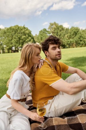 Photo for A stylish young couple, elegantly dressed, relaxes on a blanket in a lush park setting, embodying a luxurious lifestyle. - Royalty Free Image