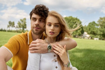 A stylish man and woman are striking a pose together in a lush green field, exuding grace and sophistication.