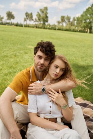 Foto de A beautiful young couple in elegant attire relaxes on a blanket in a park, exuding old money class while enjoying each others company. - Imagen libre de derechos