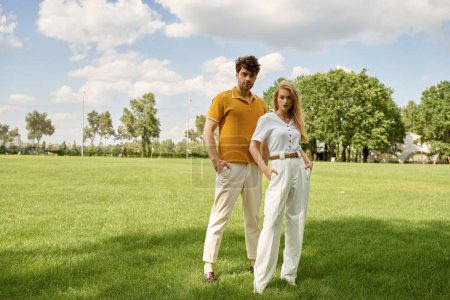 Una hermosa pareja joven, vestida elegantemente, de pie juntos en un campo verde exuberante, exudando un sentido de lujo rico en dinero antiguo.