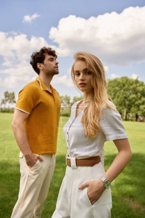 A stylish man and woman embrace in a lush green field, embodying an affluent and timeless connection with nature.