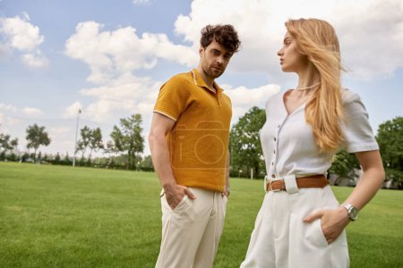 Foto de Un hombre y una mujer elegantes vestidos con ropa elegante se unen en un campo verde exuberante, que encarna un estilo de vida de lujo. - Imagen libre de derechos