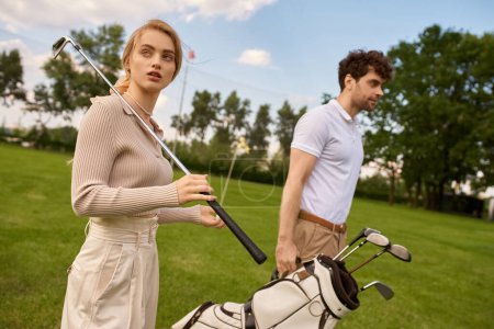 Foto de Un hombre y una mujer joven con estilo en traje elegante caminar tranquilamente en un campo de golf verde exuberante, disfrutando de la compañía de los demás. - Imagen libre de derechos