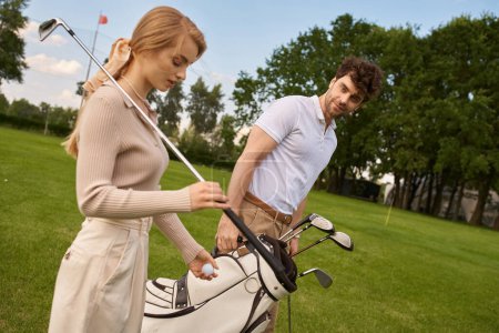 Foto de Un hombre y una mujer en traje elegante se paran juntos en un campo de golf exuberante, encarnando una exhibición refinada de ocio y sofisticación. - Imagen libre de derechos
