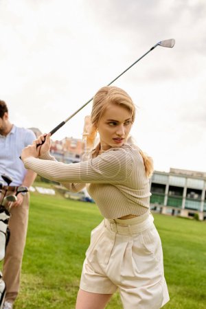 A woman in elegant attire swings a golf club in front of a man on a green field, embodying an upper-class pastime.