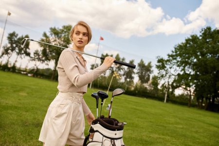 Young woman in stylish attire holds a golf bag on a lush green field at an upper-class golf club.