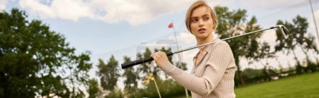 Foto de A young woman in elegant attire skillfully swings a golf club on the green field during a leisurely outing. - Imagen libre de derechos