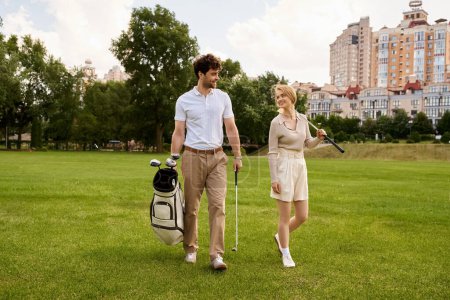 Foto de Una joven pareja en un elegante atuendo caminan tranquilamente a través de un exuberante campo de golf verde, disfrutando de una lujosa experiencia al aire libre juntos.. - Imagen libre de derechos