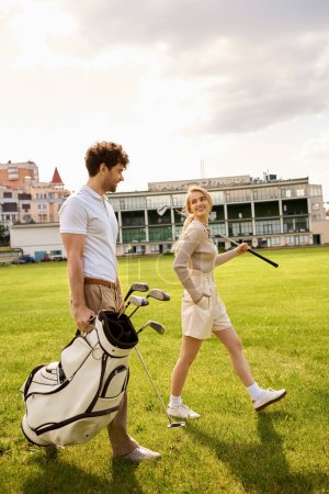 A man and woman in elegant attire walking casually on a grassy field with golf clubs in hand.