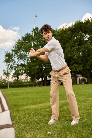 Foto de Un joven con elegante atuendo balancea un club de golf en un campo verde, encarnando el estilo de vida de lujo del dinero viejo. - Imagen libre de derechos