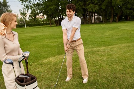 A young couple, elegantly dressed, enjoy a game of golf on a lush green field at a prestigious golf club.