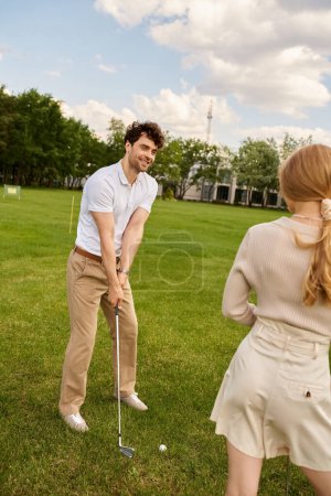 Young couple in elegant attire enjoying a round of golf on a lush green course in a luxurious setting.