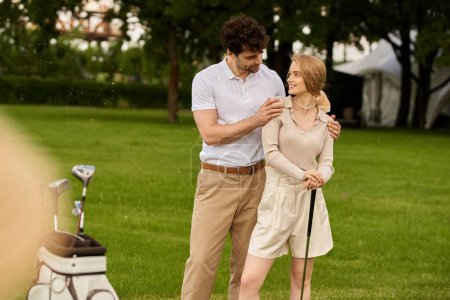 Foto de Una elegante pareja joven en un elegante atuendo de pie lado a lado en un exuberante campo de golf verde. - Imagen libre de derechos