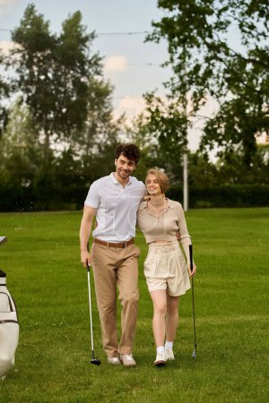 Foto de Una pareja joven y elegante caminando tranquilamente a través de un campo de golf, tomando el sol bajo el sol de un estilo de vida de clase alta. - Imagen libre de derechos