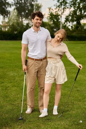 Foto de Un hombre joven y una mujer en traje elegante posan amorosamente en un campo de golf verde bajo el cielo despejado. - Imagen libre de derechos