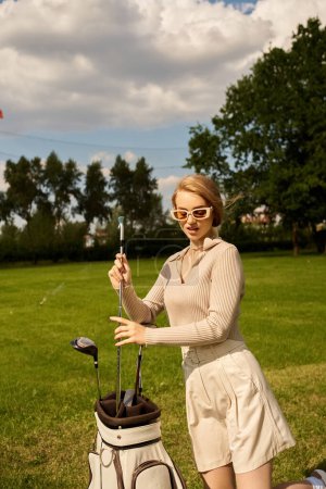 A young woman in elegant attire with her golf club in a lush park setting.