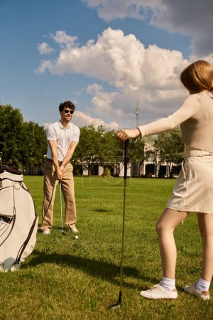 Una joven pareja vestida elegantemente jugando al golf juntos en un parque, disfrutando de un día al aire libre.