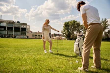 A young man and woman dressed elegantly play golf on a lush green field, enjoying a leisurely afternoon together.