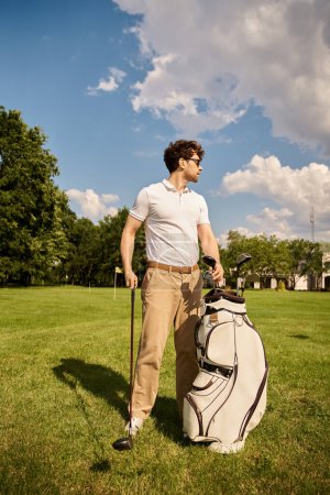 Téléchargez les photos : Un homme se tient sur un terrain herbeux avec un sac de golf, incarnant un style de vie de classe supérieure dans un élégant club de golf. - en image libre de droit