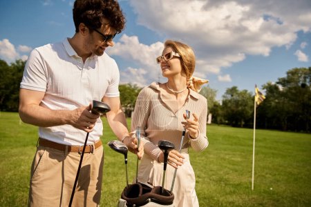 Téléchargez les photos : Un jeune couple élégant en tenue haut de gamme profite d'un jeu de golf sur un terrain verdoyant dans un club exclusif. - en image libre de droit