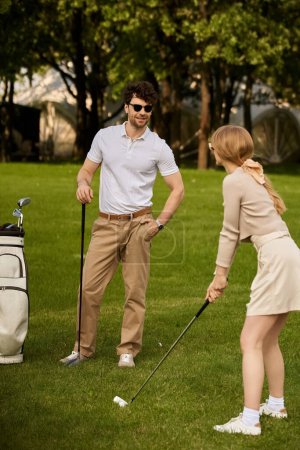 A young man and woman elegantly play golf in a park, embodying luxury and sophistication in their attire and swings.