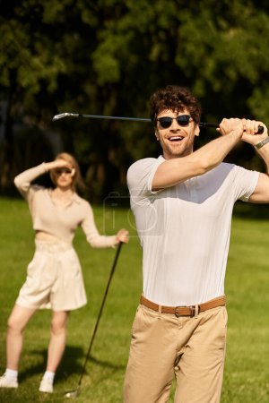 A stylish man and woman playing golf in a park, enjoying a leisurely round on a sunny day.