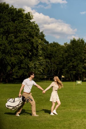 A stylish man and woman in elegant attire romantically stroll hand in hand on a lush green golf course.