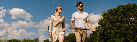 Téléchargez les photos : Un jeune couple en vêtements élégants marche sur un parcours de golf luxueux, profitant de l'atmosphère raffinée. - en image libre de droit