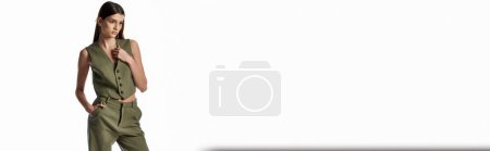Téléchargez les photos : Une femme chic avec de longs cheveux foncés pose dans une combinaison verte sur fond blanc. - en image libre de droit