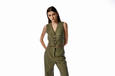 A beautiful woman with long dark hair poses in a stylish green jumpsuit against a gray backdrop, exuding elegance and sophistication.