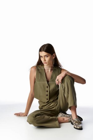 A stylish, fashionable woman with long dark hair sits cross-legged on the floor in a serene pose.
