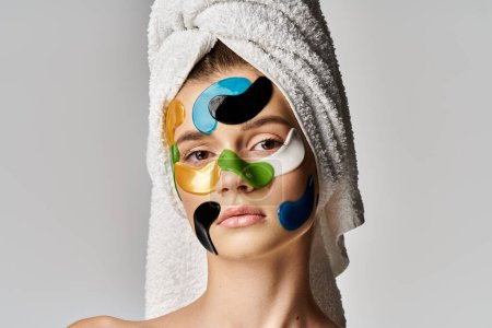 Foto de Una joven con una toalla envuelta alrededor de la cabeza con manchas en los ojos en la cara. - Imagen libre de derechos