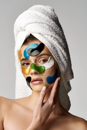 A young woman poses with a towel wrapped around her head, sporting colorful eye patches.